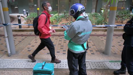 A-delivery-worker-waits-next-to-a-police-officer-outside-a-public-housing-building-placed-under-lockdown-as-he-hopes-complete-a-food-delivery-order-after-a-large-number-of-residents-tested-positive