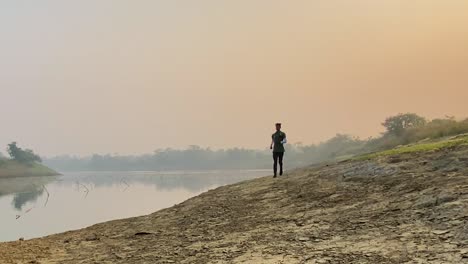 Man-running-towards-camera,-jogger-sprinting-by-river-in-Sylhet,-slow-motion