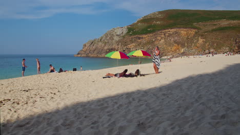 Gente-Disfrutando-De-Las-Aguas-A-Lo-Largo-De-La-Costa-Y-Relajándose-Bajo-Una-Sombrilla-En-La-Playa-De-Porth-En-Cornualles,-Inglaterra,-Reino-Unido