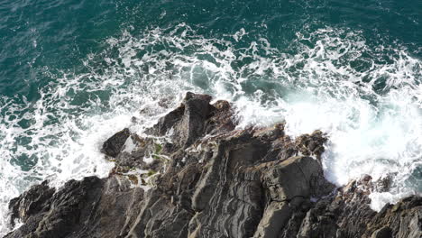 Top-down-aerial-view-of-ocean-waves-crashing-onto-a-rocky-shoreline