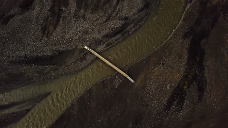 Aerial-drone-view-of-people-crossing-a-bridge,-over-a-river-flowing-in-the-Fimmvörðuháls-area,-Iceland