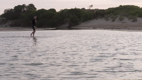 Niño-Camina-A-Través-De-Aguas-Tranquilas-Y-Poco-Profundas-Del-Río-Al-Atardecer,-Cámara-Lenta