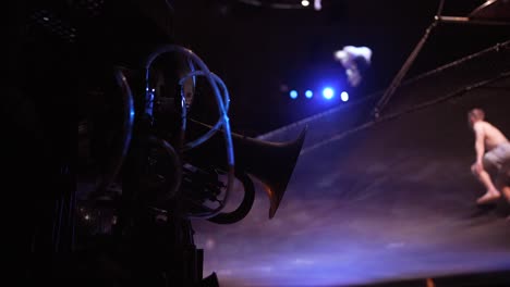 Cirque-du-Soleil:-Professional-circus-athletes-practicing-and-rehearsing-trampoline-act-in-a-stunning-dimmed-light-venue,-statue-in-the-foreground