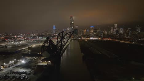 Vista-Aérea-Sobre-Un-Puente-De-Línea-Ferroviaria,-Que-Revela-La-Estación-De-Tren-Amtrak-Y-El-Nebuloso-Horizonte-Nocturno-De-Chicago