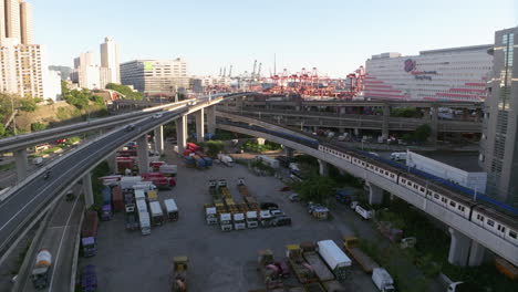 Aerial-forward-shot-of-Tsuen-Wan-line-MTR-train-and-industrial-port-with-cranes-in-background---Hong-Kong,Asia