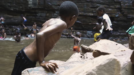 Kinder-Spielen-Im-Wasser-Nahaufnahme-Eines-Schwarzen-Kleinkindes,-Das-In-Natürlicher-Umgebung-Auf-Einen-Felsen-Klettert