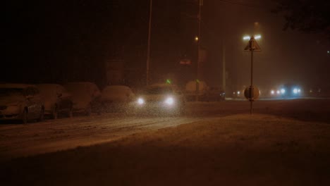 Lone-car-driving-in-the-city-on-a-frosty-winter-night-during-a-blizzard,-warm-lights