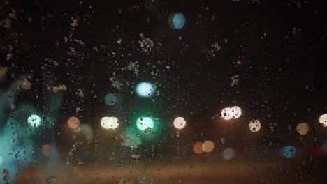 Snowflakes-falling-on-the-window,-melting,-blurred-city-lights-in-the-background