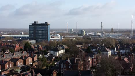 Aerial-view-over-park-trees-to-industrial-townscape-with-Pilkingtons-blue-head-office,-Merseyside,-England