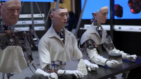 A-Row-of-Humanoid-Robots-With-Hyperrealistic-Faces-Seated-in-Front-of-a-Long-Table-Motionless-in-Gentle-Monster-Store-in-Starfield-Hanam