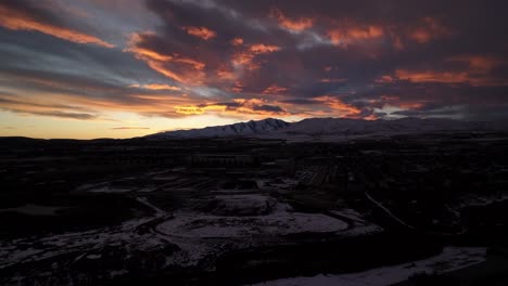 Stunning-sunset-over-a-community-in-the-valley-below-snowy-mountains---aerial