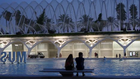 Couple-at-The-City-of-Arts-and-Sciences,-paddle-boarding-in-Valencia,-Spain,-Summer-evening