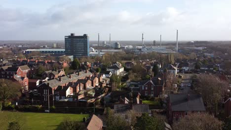 Aerial-view-pan-across-park-trees-to-industrial-townscape-property-with-blue-skyscraper,-Merseyside,-England