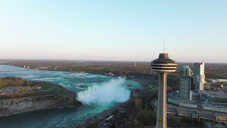 Cataratas-Del-Niágara-Desde-El-Lado-De-Canadá-Con-Torre-De-Observación-Durante-La-Puesta-De-Sol,-Descenso-De-Drones