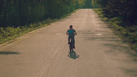 Young-boy-riding-a-bicycle-on-the-road-through-nature