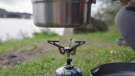 Poner-Una-Olla-En-La-Cocina-De-Campo-En-La-Orilla-Del-Lago-Durante-Un-Día,-Preparación-De-Alimentos