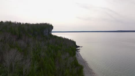 Bruce-peninsulacliffs,-Ontario,-Canada-in-early-spring-and-lake-Huron,-Drone-flies-nearby-towards-the-sun