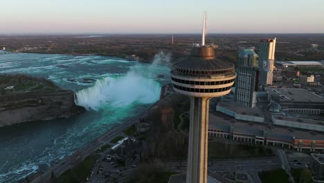 Las-Cataratas-Del-Niágara-Desde-El-Lado-De-Canadá-Con-La-Torre-De-Observación-Durante-La-Puesta-De-Sol,-El-Dron-Vuela-De-Lado