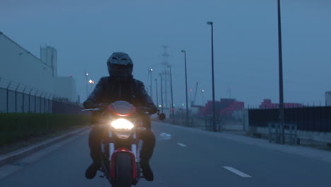 Anamorphic-footage-of-a-young-male-motorcyclist-cruising-on-a-red-sporty-motorcycle-in-an-industrial-zone-at-night