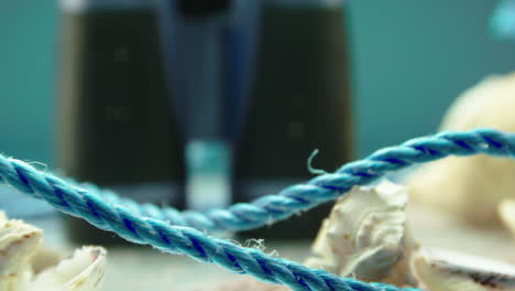 Close-up-video-of-a-blue-rope-and-sea-shells,-surrounded-by-beach-sand,-on-a-turntable-display-with-binoculars-in-the-background