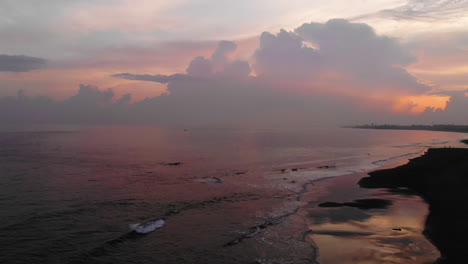 Aerial-footage-of-a-sunset-at-the-beach,-cloudy-sky,-orange-tints,-ocean-waves