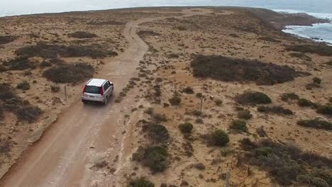 A-lone-4WD-explores-a-rocky-outcrop-by-the-ocean,-aerial-follow-shot