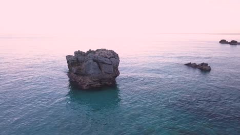 4K-Aerial-forward-drone-shot-of-a-big-rock-in-the-calm-sea-during-blue-hour-in-Greece