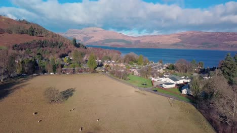 Reveal-drone-shot-of-Luss-in-the-Highlands-of-Scotland-and-in-the-background-Loch-Lomond-during-golden-hour