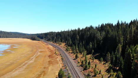 Aerial-flight-over-mountain-railroads-Flying-over-a-dried-up-lake,-now-a-grassy-field