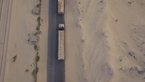 Fly-backwards-over-a-long-line-of-trucks-in-the-desert-over-a-cracked-road