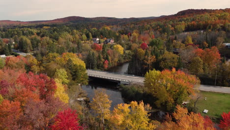 Colorful-road-bridge,-revealing-houses-in-middle-fall-foliage-of-Canada