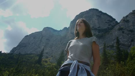 Girl-standing-proud-with-mountains-and-forest-behind-her,-up-shot,-slow-motion