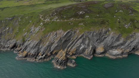 Drone-Panning-Lateralmente-Mostrando-Acantilados-Rocosos-En-Detalle-Por-El-Mar-Azul-Verdoso-Irlandés