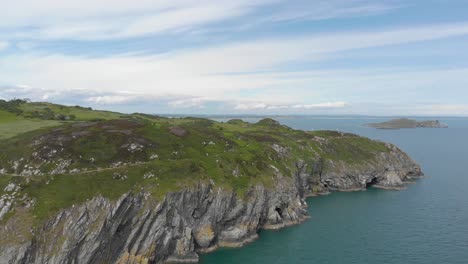 Vista-Panorámica-De-Acantilados-Y-Montañas-Y-Una-Isla-Junto-Al-Hermoso-Mar-Azul-Verdoso-Irlandés-En-Un-Día-Soleado