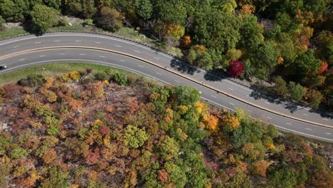 An-aerial-view-high-above-a-curved-mountain-road-in-upstate-NY-during-the-fall-foliage-changes-on-a-beautiful-day