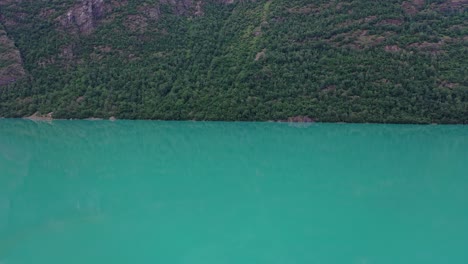 Oldevatn-freshwater-lake-in-Sogn-Nordfjord-Norway---Slow-downward-moving-aerial-with-screen-split-between-mountainside-and-lake-in-middle---Vibrant-green-glacial-water