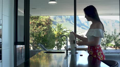 Girl-adding-milk-to-coffee-and-stirring-in-modern-kitchen-with-beautiful-scenery-in-the-background
