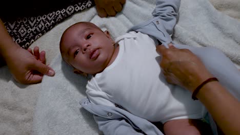 Parents-Dressing-Cute-2-Month-Old-Indian-Baby-Boy-As-He-Lays-On-Blanket-On-The-Floor