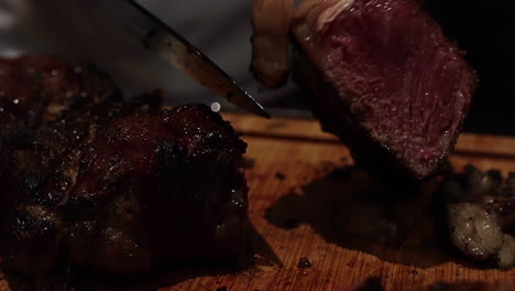 Fork-and-knife-carve-delicious-thick-juicy-cooked-rare-steaks-on-wooden-chopping-block,-close-up