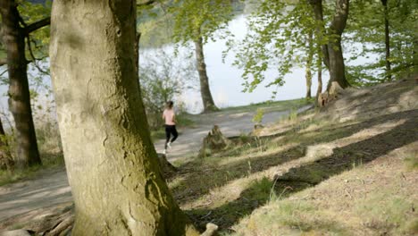 Woman-running-through-woods-near-river-viewed-from-behind-tree