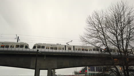 Small-train-passing-over-a-small-bridge-on-a-somber-day,-grey-skies-in-background
