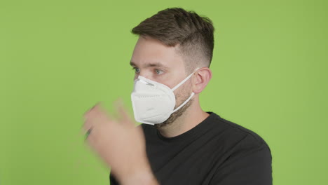 Man-Puts-on-Protective-KN95-Face-Mask-While-Looking-Left-of-Camera-on-Green-Screen-Chroma-Key