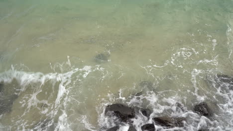 Turquoise-ocean-waves-breaking-on-sandy-and-rocks-coastline