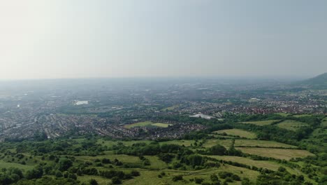Aerial-drone-shot-over-meadows-and-fields-with-view-of-a-city-and-haze-on-horizon