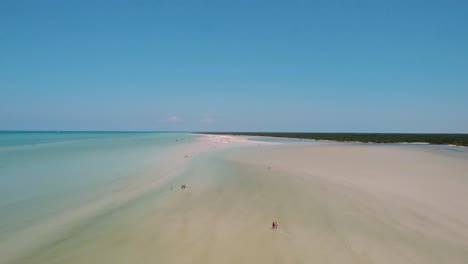 Aerial-flyover-of-sandy-beach-in-Isla-Holbox-Mexico,-people-sunbathe-on-exotic-beach-with-white-sand-and-shallow-water