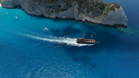 Drone-Shot-Tracking-a-pirate-Ship-and-revealing-an-old-Shipwreck,-Zakynthos,-Greece,-4k-UHD