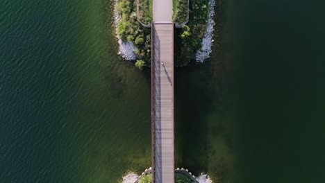 A-balanced-aerial-shot-of-woman-running-across-a-small-bridge-spanning-a-lake
