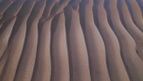 Wave-pattern-of-sandy-desert-with-water-overflowing-it,-aerial-drone-shot