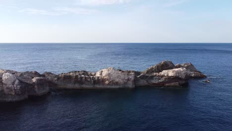 Rocas-Irregulares-Cubiertas-De-Musgo-Dividen-El-Mar-Azul-Profundo