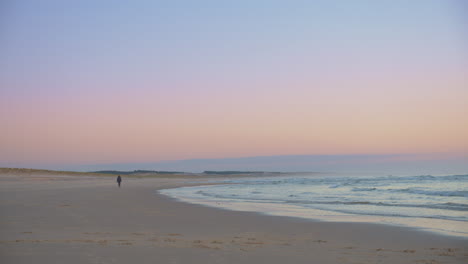 Establishing-Cinematic-Shot-of-Person-Walking-Alone-During-a-Colorful-Sunset-on-a-Beach-Slow-Motion